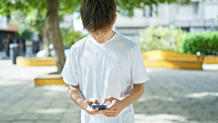 A young man focused on his smartphone in a sunlit urban park, exemplifying modern outdoor...