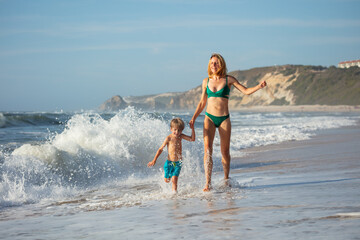 Woman and young boy having fun in ocean waves at a sandy beach