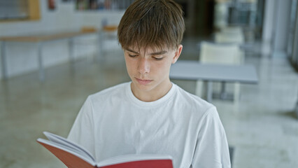 Caucasian teenage boy reading book at university library table