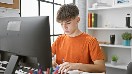 Focused teenage boy studying at a modern home desk setup, with a computer and notebooks