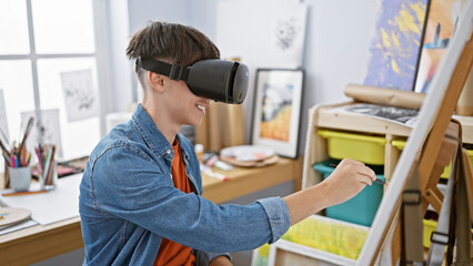 A young man interacting with virtual reality equipment while painting in a bright, modern studio...