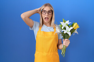 Young caucasian woman wearing florist apron holding flowers crazy and scared with hands on head,...