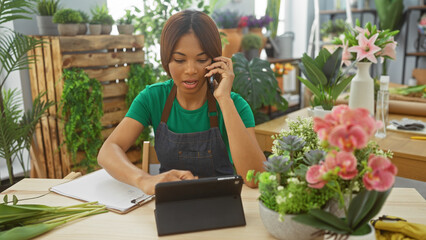 African american woman florist multitasking, talking on phone and using tablet in flower shop