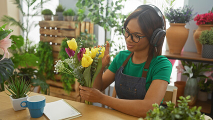 African american woman florist arranging colorful tulips in a green indoor shop with plants and...