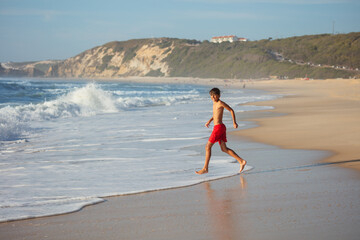 An active teenager dashes across the shoreline, with sea foam