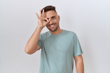 Fototapeta premium Hispanic man with beard standing over white background doing ok gesture with hand smiling, eye looking through fingers with happy face.
