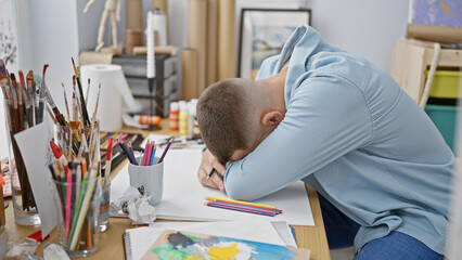A young man expressing frustration or exhaustion in a creative studio setting surrounded by art...