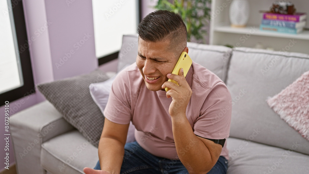 Sticker Handsome, worried latin guy in serious phone talk, upset at home. unhappy young man speaking on smartphone, sitting on living room sofa, deep in conversation, addressing problems