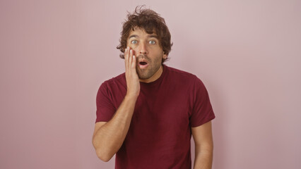 Surprised young hispanic man with a beard and maroon shirt against a pink isolated background.