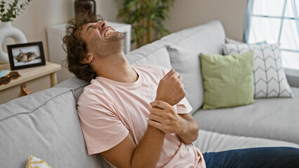 Laughing hispanic man comfortably relaxes on a sofa in a cozy living room