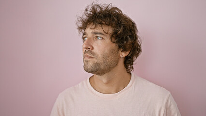 Handsome hispanic man with curly hair posing thoughtfully against a plain pink background