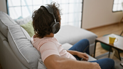 A relaxed man with headphones sits on a couch in a modern living room, enjoying leisure time.
