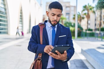 Young latin man business worker using touchpad with serious expression at street