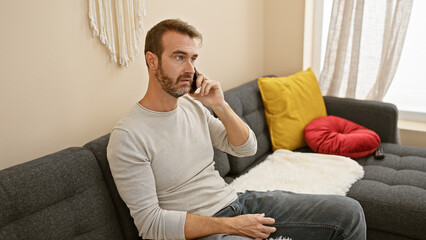 A middle-aged hispanic man with a beard talks on the phone in a cozy living room setup, adding a personal touch to the indoor scene.