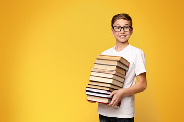 A young boy standing and holding a stack of books in his arms.