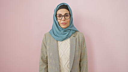 Portrait of a mature woman with hijab and glasses against a pink background, exuding confidence and...