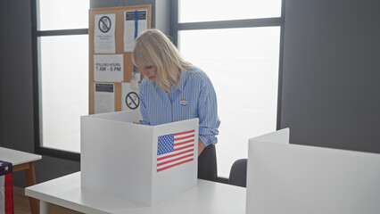A young blonde woman in a striped shirt casts her ballot at an american polling station,...