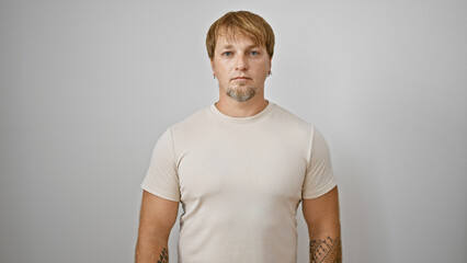 Portrait of a young adult man with blond hair and beard, tattooed arms, wearing a beige t-shirt,...
