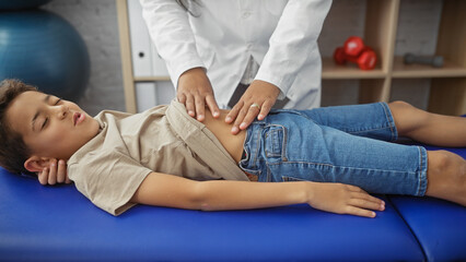 A woman physiotherapist treating a young boy patient in a rehab clinic room, with focus on care and...