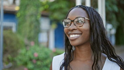 Portrait of a smiling young adult african american woman with curly hair wearing glasses outdoors...