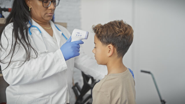 A female doctor in a clinic checks the temperature of a young boy patient with a digital thermometer, depicting healthcare.