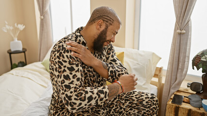 Bearded african american man in stylish pajamas feeling shoulder pain in a modern bedroom