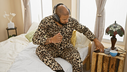 A handsome african american man in a leopard print pajama relaxes with music in a well-lit bedroom,...