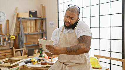 A focused bearded man talking on the phone while taking notes in a carpentry workshop.