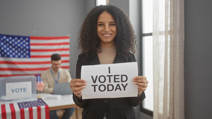 A woman holding a 'i voted today' sign proudly in an indoor voting center with american flags and...