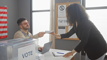 A woman hands a ballot to a man at a usa polling station with an american flag in the background.