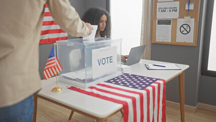 Man voting in presence of woman at a us electoral college with american flag and ballot box indoors.