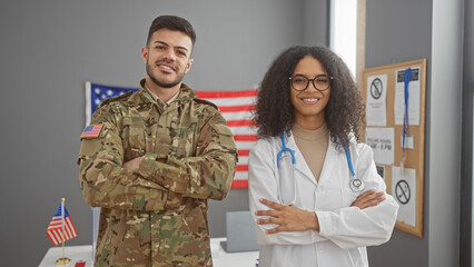 A man in military uniform and a woman doctor standing with arms crossed in front of a usa flag,...