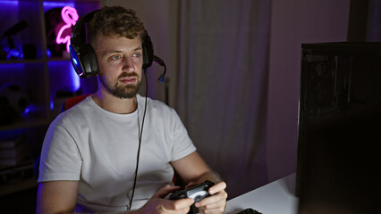 Caucasian man with beard and headphones playing video games in a dark room at night