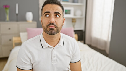 Pensive hispanic man with beard in a modern bedroom interior contemplating.