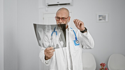 Mature bearded man in white lab coat examines x-ray in bright hospital room, portraying healthcare...