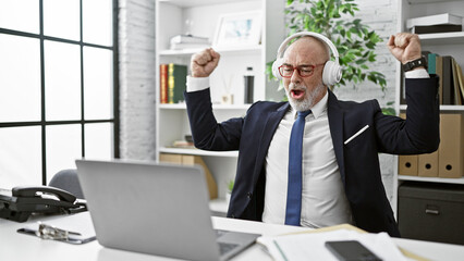 Euphoric senior man with headphones celebrating in a modern office setting