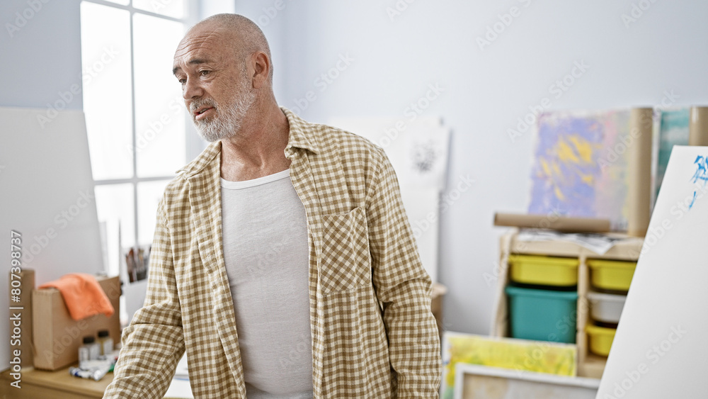 Wall mural a mature man with grey hair stands thoughtfully in a bright art studio, reflecting creativity and le