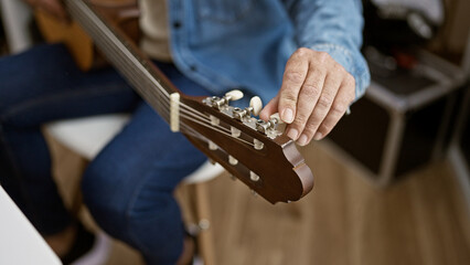 Close-up of a mature man's hands tuning a guitar in a casual indoor setting.