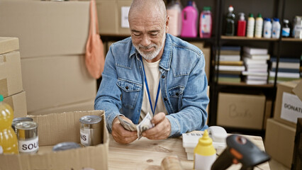 A mature man counts money at a donation center surrounded by boxes and supplies.