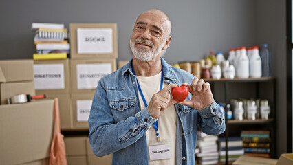 Smiling man holding heart volunteering in warehouse filled with donation boxes.