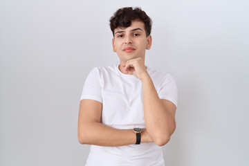 Young non binary man wearing casual white t shirt with hand on chin thinking about question,...