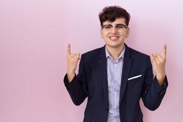 Young non binary man with beard wearing suit and tie shouting with crazy expression doing rock symbol with hands up. music star. heavy concept.