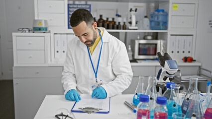 Hispanic scientist man writes research notes in a laboratory with microscope and vials