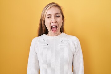 Young caucasian woman wearing white sweater over yellow background winking looking at the camera with sexy expression, cheerful and happy face.