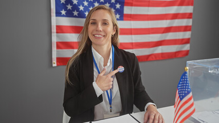 A smiling young caucasian woman points to her 'i voted' sticker in an american indoor voting center...