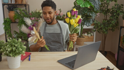 A friendly african american man arranges tulips during a video call in a vibrant indoor flower shop.