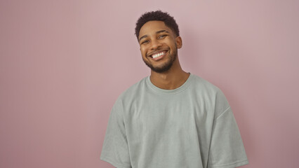 A smiling african american man in a casual grey shirt posing against an isolated pink background,...