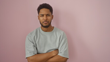 Handsome adult black man with arms crossed standing against an isolated pink wall, portraying...