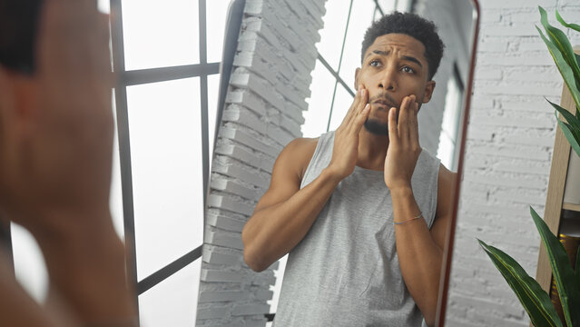 Concerned african man inspecting his face in mirror at modern apartment