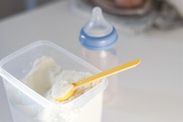 Dry powder formula milk for feeding babies in a can with yellow plastic scoop and empty feeding bottle
